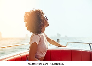 Smiling young woman wearing sunglasses enjoying the fresh sea air and ocean view while sitting on a boat during summer vacation