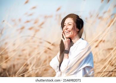 Smiling young woman in white blouse standing in field dry pampas grass in front of sky. Style and fashion. Girl in casual outfit enjoying sunlight. Golden hour. Boho style.