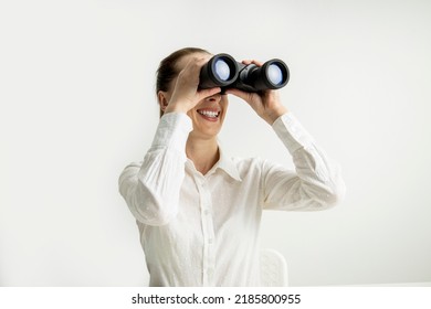 Smiling young woman in white shirt looking through binoculars on white background. - Shutterstock ID 2185800955