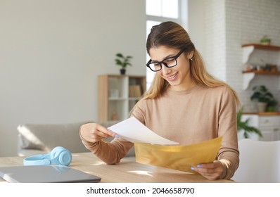 Smiling young woman who is excited by good news reads letter unfolded from paper envelope. Excited future female student receives decision from commission regarding her admission to university. - Shutterstock ID 2046658790