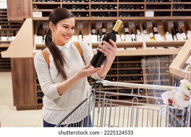 Smiling Young Woman As A Wine Connoisseur Reading Label On Bottle Of Wine In Supermarket