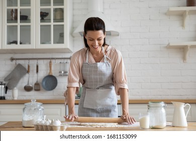 Smiling Young Woman Work With Wooden Roller Pin Making Sweet Pie Or Pastry Dough In Kitchen, Happy Millennial Female Loving Wife Cooking In Apron Preparing Family Dinner Or Dessert Baking Buns