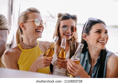 Smiling Young Women Drinking Beer At Beach Bar