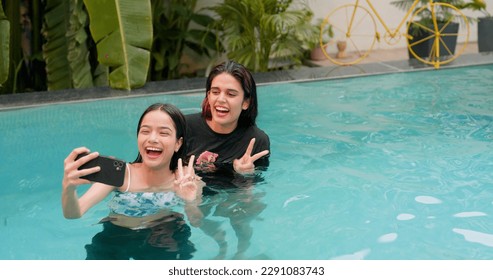 Smiling young women standing taking selfie in swimming pool with female friend through mobile phone. Indian girls making self portrait photos on smartphone. Models showing positive emotion - Powered by Shutterstock