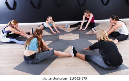 Smiling Young Women Training Yoga Positions, Sitting In Circle In Modern Yoga Studio