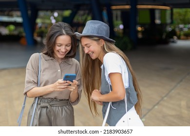 Smiling Young Women Watching Photos Or Video On Smartphone In Shopping Mall. Teenage Friends Meeting And Talking At Weekend. Social Networking And Youth Culture Concept