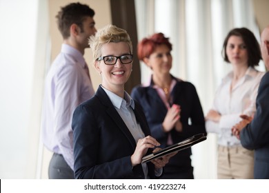 Smilling Senior Older  Business Woman With Tablet Computer  In Front Her Team Blured In Background. Group Of Young Business People At Modern Bright  Startup Office Interior.