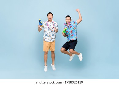 Smilng Happy Asian Male Friends Playing With Water Guns And Jumping In Blue Isolated Background For Songkran Festival In Thailand And Southeast Asia