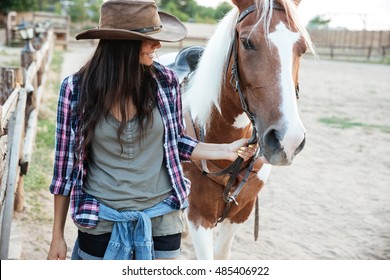 Smilng lovely young woman cowgirl with her horse in village