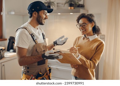 Smilng young woman signing document while communicating with handyman at the kitchen - Powered by Shutterstock