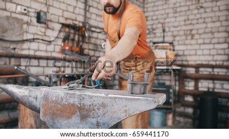 The smith knocks on a hot rod with a hammer