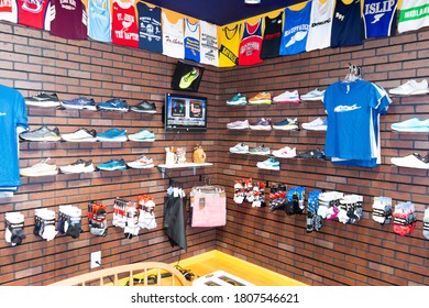 Smithtown, New York, USA - 28 August 2020: Running Shoes Are On Display With Clothing And Uniform Tops Hanging On The Wall At A Local Running Shoe Store.