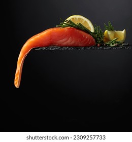 Smocked salmon with rosemary, lemon, and peppercorn on a black background. Copy space. - Shutterstock ID 2309257733