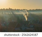 Smog and smoke hover over the town at sunrise. A city panorama reveals streets, townhouses, and houses. Smoke from chimneys is caused by the burning of coal or other materials in home heaters.