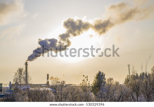 The smoke from the chimneys of the boiler house in\
winter at sunset
