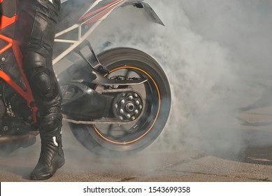 The smoke comes out from under the wheels. Motorcycle wheel closeup. Smoke due to tire rubbing against asphalt. The rider prepares to do the trick on the motorcycle. Burned rubber on the road.