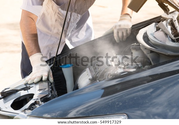 Smoke coming out\
the engine. Professional mechanic checking car engine in standing\
on the road,Broken car\
concept