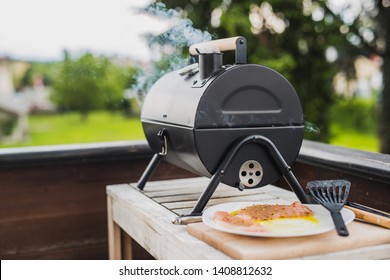 Smoke Coming Out Of A Smokestack Of A Small Black Smoker Grill Or Barbecue On Green Background.