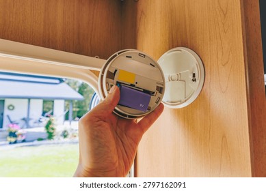Smoke detector battery replacement inside a modern caravan with natural light and wood panels