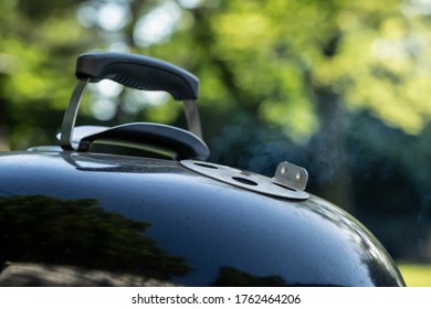 Smoke escapes from the vent of a kettle style barbecue grill.  - Shutterstock ID 1762464206