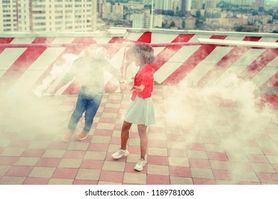 Smoke everywhere. Cheerful young loving couple having wonderful time on the roof while being surrounded by a white smoke from the smoke flare - Powered by Shutterstock