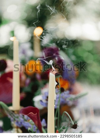 Smoke from an extinguished white candle. In the background are red and purple tropical flowers, burning candles. Floral decor.