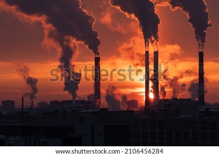 Smoke from heating station in big city during winter season at sunset. Smokestack pipes emitting co2 from coal thermal power plant into atmosphere. Air pollution and emission ecology problem concept