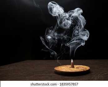 Smoke on dark background from smoldering burning cone incense standing on wooden incense holder