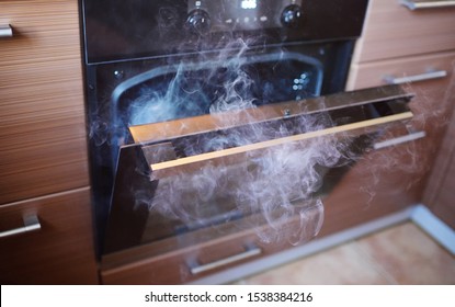The Smoke From The Oven In The Kitchen Closeup. Burnt Food.Blurred Image Of The Oven With Focus On The Door Handle.