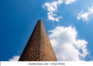 Smoke Stack Of Ruined Old Factory With Rusty Iron Steps Leading Upwards To The Vanishing Point And Red Bricks On A Sunny Day With Cloudy Blue Sky