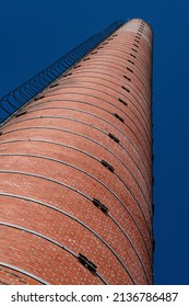 Smoke Stack Of Ruined Old Factory With Iron Steps Leading Upwards To The Vanishing Point And Red Bricks On A Sunny Day With Cloudy Blue Sky.