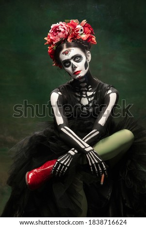 Smoke. Young girl like Santa Muerte Saint death or Sugar skull with bright make-up. Portrait isolated on dark green studio background with copyspace. Celebrating Halloween or Day of the dead.