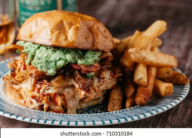 Smoked Bbq Chicken Sandwich With Sautéed Onions, Bacon, Pepper Jack Cheese And Guacamole Spread On Rustic Background