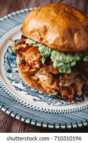 Smoked Bbq Chicken Sandwich With Sautéed Onions, Bacon, Pepper Jack Cheese And Guacamole Spread On Rustic Background