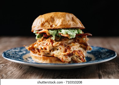 Smoked Bbq Chicken Sandwich With Sautéed Onions, Bacon, Pepper Jack Cheese And Guacamole Spread On Rustic Background