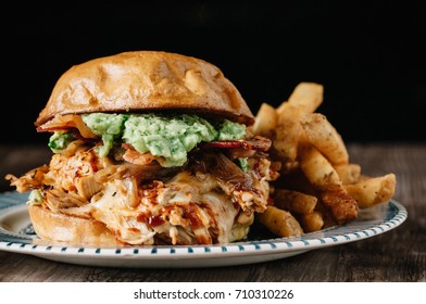 Smoked Bbq Chicken Sandwich With Sautéed Onions, Bacon, Pepper Jack Cheese And Guacamole Spread On Rustic Background