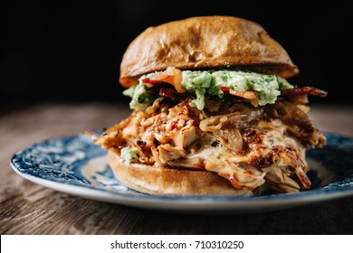 Smoked Bbq Chicken Sandwich With Sautéed Onions, Bacon, Pepper Jack Cheese And Guacamole Spread On Rustic Background