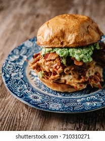 Smoked Bbq Chicken Sandwich With Sautéed Onions, Bacon, Pepper Jack Cheese And Guacamole Spread On Rustic Background