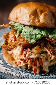 Smoked Bbq Chicken Sandwich With Sautéed Onions, Bacon, Pepper Jack Cheese And Guacamole Spread On Rustic Background