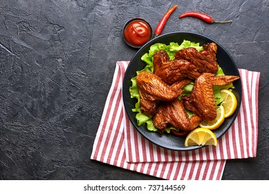 Smoked Chicken Wings With Ketchup And Chili Hot Peppers. Black Concrete Background. Barbecue. Top View. Space For Text.