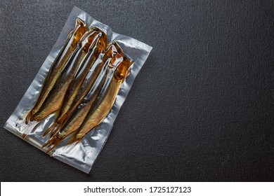 Smoked herring fish, in a vacuum transparent package, on a black background