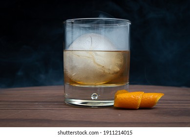 Smoked Old Fashioned With A Spherical Ice Cube On A Wooden Table