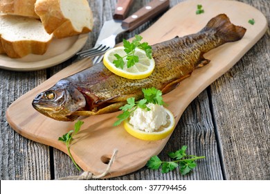 A smoked rainbow trout served on a wooden cutting board with horseradish, parsley, lemon  and baguette