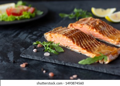 Smoked red fish fillet, trout or salmon steaks served on slate board with lemon and rocket salad 