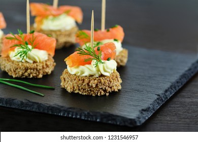 Smoked salmon canapes with cheese cream and dill on brown bread over black slate platter