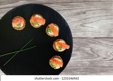 Smoked Salmon Canapes With Cheese Cream And Dill Served On Round Black Slate Platter Over Wooden Background, Top View, Overhead