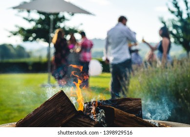 Smokey outdoor fire pit with people gathered together at a party restaurant function in the background.