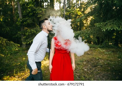 Smoking businessman kissing beautiful young blonde girl with innocent kind face, piercing, eyes closed, red lips, dress with decollete. Clouds of thick smoke. Electronic cigarette. Odd lovers feelings
