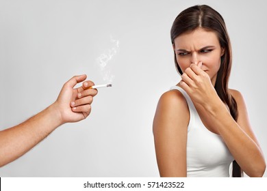 Smoking. Closeup Of Beautiful Unhappy Woman Turning Away In Negative Reaction On Someone Smoking. Portrait Of Healthy Female Holding Nose, Doesn't Like Smelling Bad Cigarette Smell. High Resolution