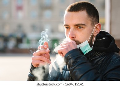 Smoking. Closeup man with mask during COVID-19 pandemic coughing and smoking a cigarette at the street. Smoking causes lung cancer and other diseases. The dangers of smoking. Coronavirus.